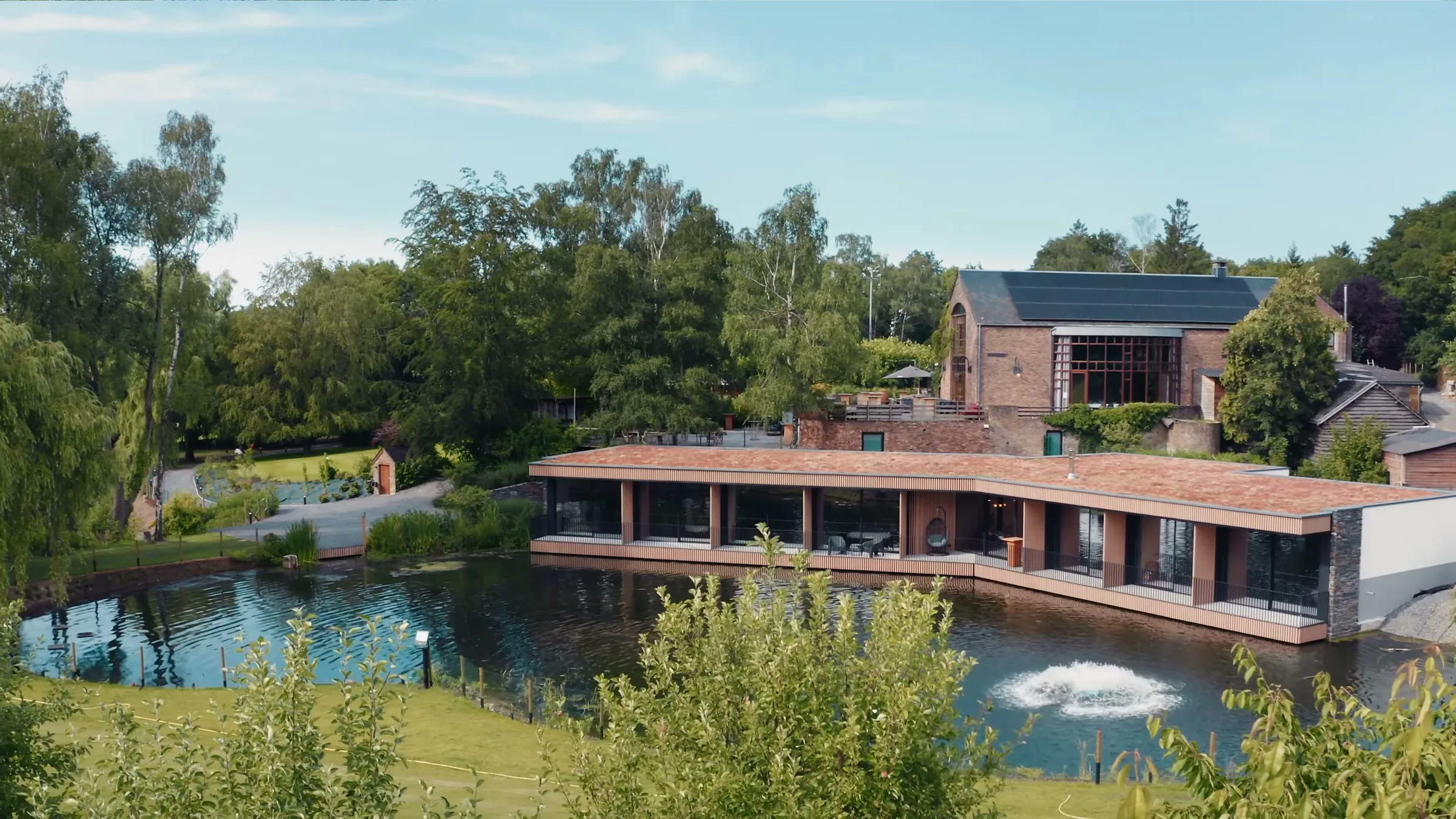 Le domaine vu du ciel : le bâtiment de pierre et de tuile posé au bord de l'étang, son jet d'eau, la prairie